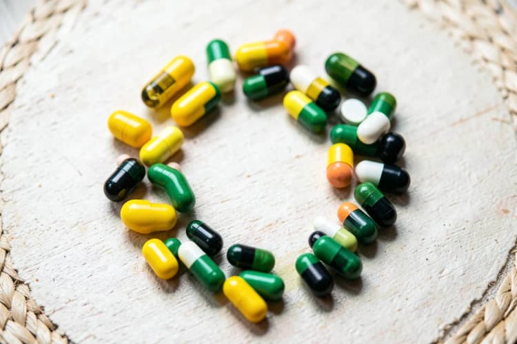 Um conjunto de diferentes vitaminas em cápsulas e comprimidos dispostos em círculo sobre uma superfície clara.